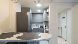 A modern kitchen with grey cabinets, a white countertop, and a dining area with a round table and stools. - Le Roxane joli cocon avec petit terrasse (Cannes)