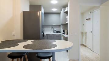 Una cocina moderna con armarios grises, una encimera blanca y una zona de comedor con una mesa redonda y taburetes.