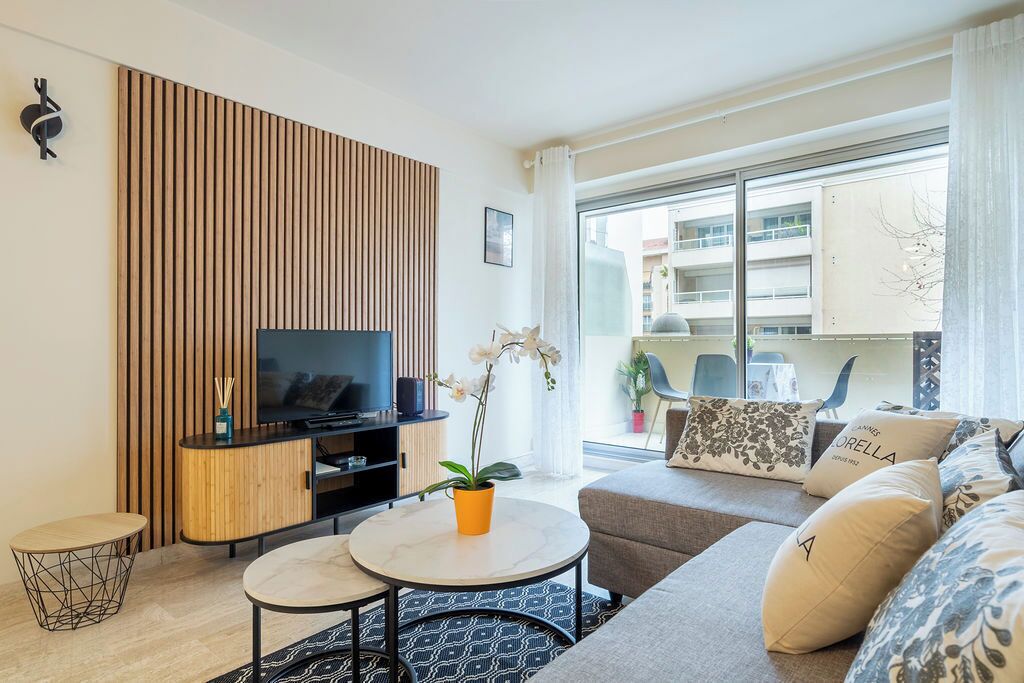 Un salon moderne avec un téléviseur à écran plat, un mur recouvert de panneaux en bois, un canapé, une table basse et un pot d’orchidée.