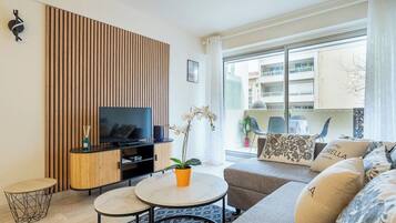 Un salon moderne avec un téléviseur à écran plat, un mur recouvert de panneaux en bois, un canapé, une table basse et un pot d’orchidée.