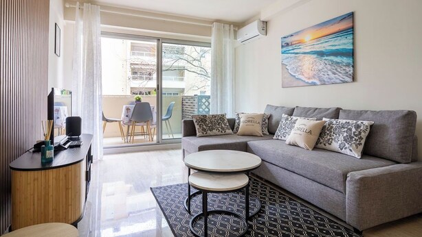 A modern living room with a grey sofa, a small round table, and a painting of a sunset. - Le Roxane joli cocon avec petit terrasse (Cannes)