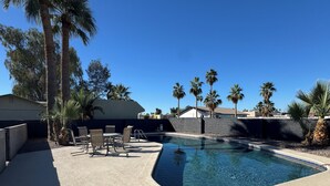 Une piscine à bords incurvés, entourée de palmiers et agrémentée d’un patio avec des chaises et des tables.