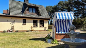 A house with a sloped roof, a small porch, and a garden with a bird sculpture, a fountain, and a striped awning. - "achterhus Usedom" Baltic Sea Idyll in the House on the Water (Zempin)