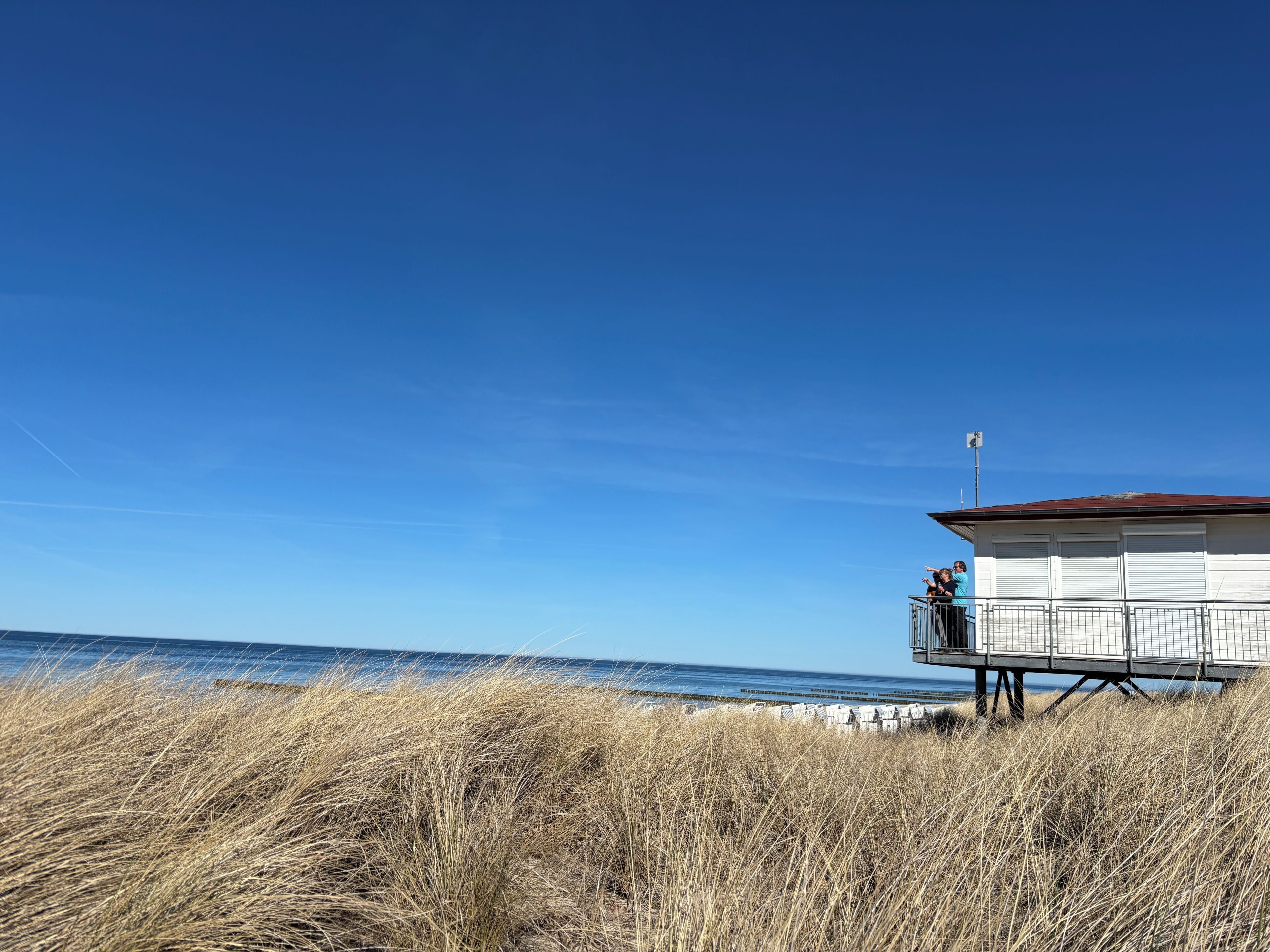 A lifeguard tower with a metal railing and a red roof, overlooking a beach with dry grass in the foreground.