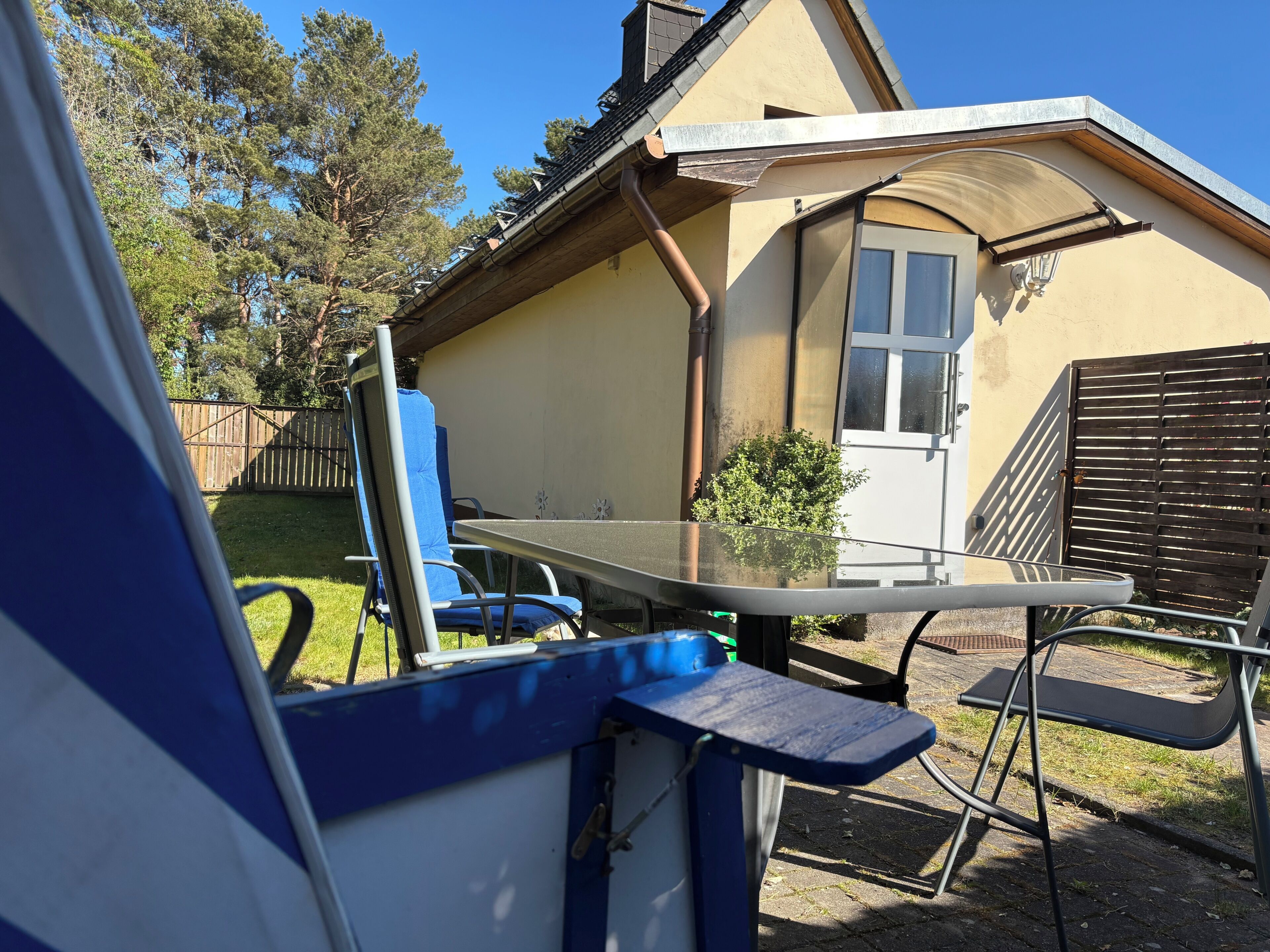 A house with a glass table and chairs, a wooden fence, and a clear sky.