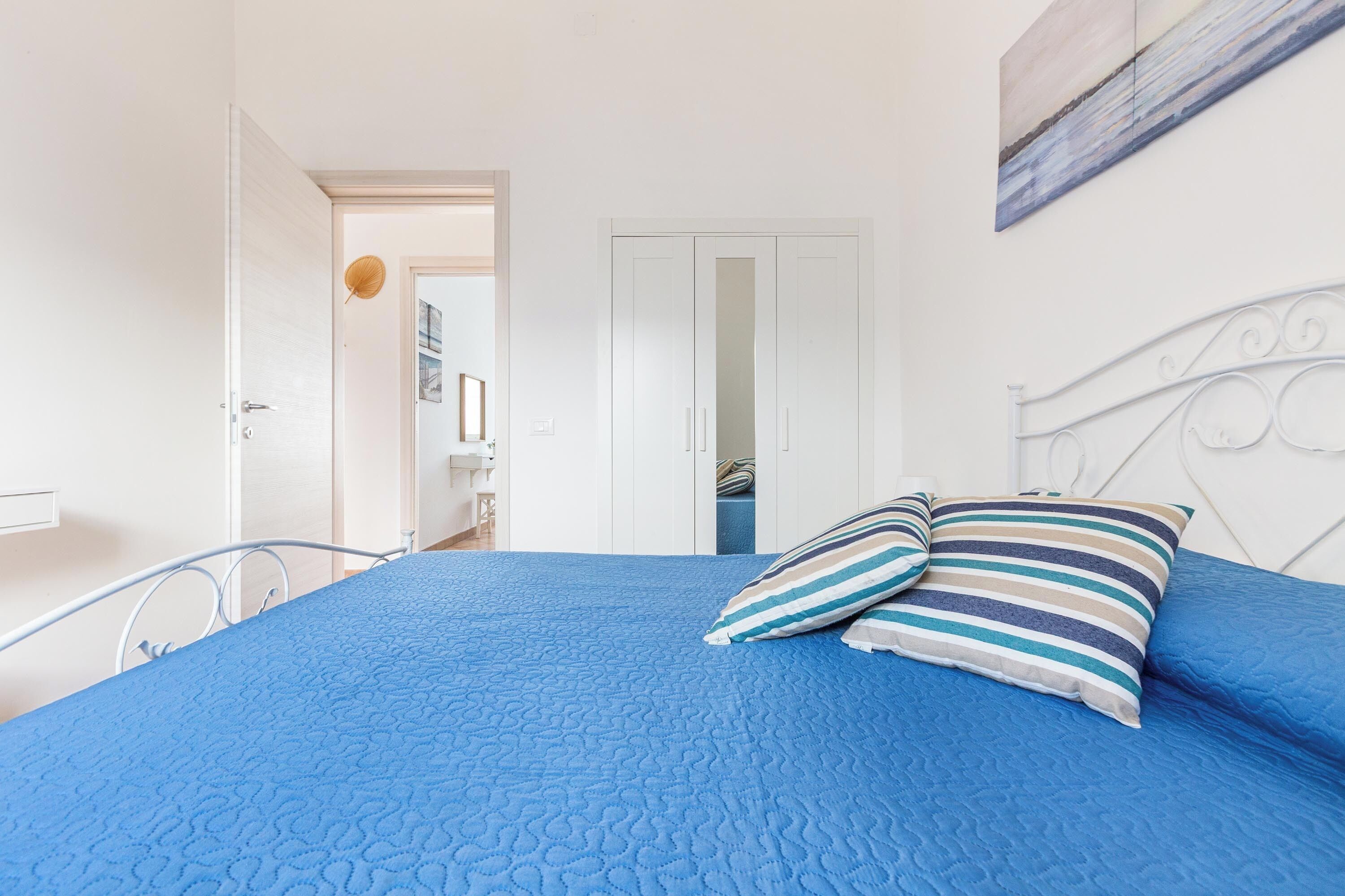 Ein Schlafzimmer mit blauer Bettdecke, einem weißen Metall-Kopfteil und gestreiften Kissen.