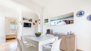 Una cocina moderna con muebles blancos, una mesa de comedor con sillas y un frutero.