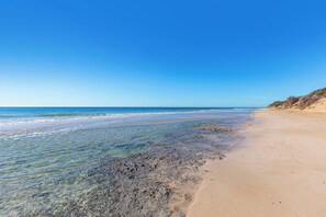 A beach with clear water, sandy shore, and a distant cliff. - Villetta Le Mar by BarbarHouse (San Pietro in Bevagna)