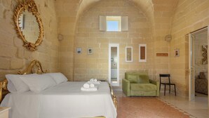 A bedroom with a bed, a green armchair, a mirror, and a stone wall. - Acamya by BarbarHouse (Acaya)