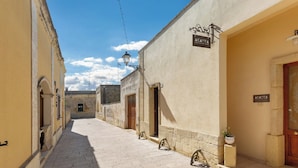 A narrow street with buildings on either side, a clear sky, and a sign for 'ACAMYA'. - Acamya by BarbarHouse (Acaya)