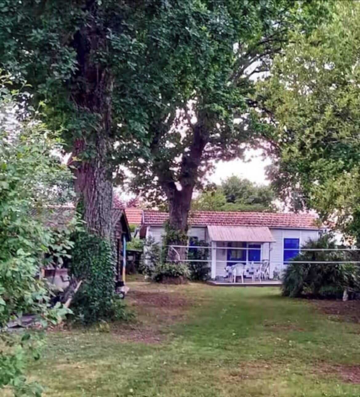 Een huis met een rood pannendak, omgeven door een verzorgd gazon en grote bomen.