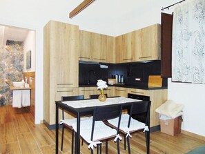 A compact kitchen with wooden cabinets, a black countertop, and a dining table with chairs. - Comfortable family cottage in the midst of nature (San Cataldo)