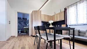 A modern kitchen with wooden cabinets, a dining area with a black table and chairs, and a view of a bathroom with a shower and sink. - Comfortable family cottage in the midst of nature (San Cataldo)