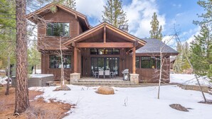 Une cabane en bois dotée d’une grande véranda, de nombreuses fenêtres et d’une cheminée en pierre.