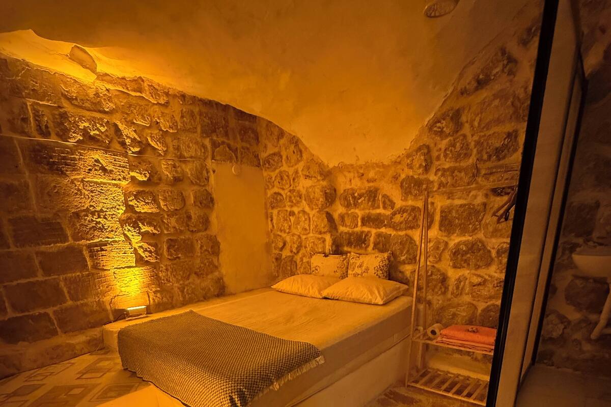 A small, stone-walled bedroom with a single bed, a nightstand, and a small table.