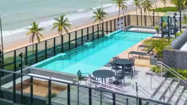 A rooftop pool with a view of the beach and ocean, surrounded by palm trees and lounge chairs. - LM BEACH HAUS (João Pessoa)