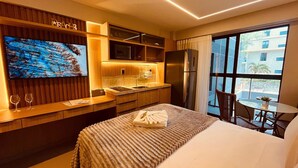 A hotel room with a bed, a TV, a kitchen area, and a balcony with a view. - LM BEACH HAUS (João Pessoa)