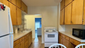 Una cocina compacta con muebles de madera, un refrigerador blanco, estufa, microondas y un comedor con mesa y sillas.