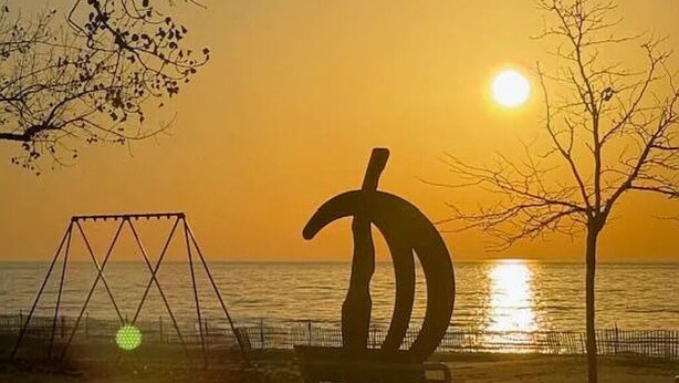 Un parque con un columpio y una escultura frente al mar durante el atardecer.