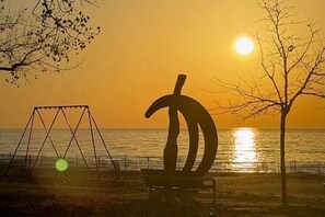 Un parc amb cadira d'oscil·lar i una escultura a la vora del mar durant el capvespre.