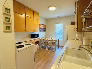 Une cuisine compacte dotée de meubles en bois, d’un four à micro-ondes, d’une cuisinière, d’un évier et d’un coin repas avec des chaises.