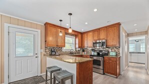 A modern kitchen with wooden cabinets, stainless steel appliances, and a large island with bar stools. - The Wright Therapy, get your beach medicine here!  NEW LISTING w/ Hot Tub! (Kill Devil Hills)