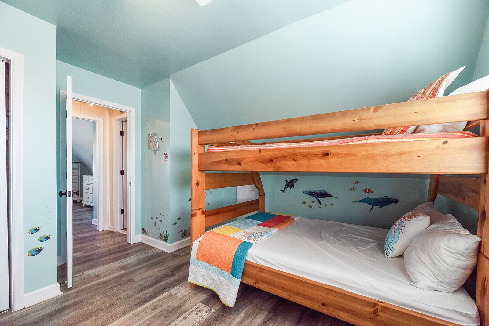Una cama litera con estructura de madera, colcha y un mural de criaturas marinas.