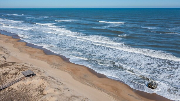 A beach with a wooden walkway leading to a building with a sloped roof. - The Wright Therapy, get your beach medicine here!  NEW LISTING w/ Hot Tub! (Kill Devil Hills)