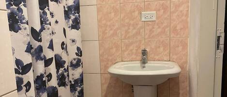 A bathroom with a sink, tiled walls, a shower curtain with a floral pattern, and a blue mat on the floor.