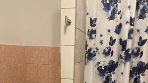 Un baño con inodoro, cortina de ducha estampada con motivos florales y un letrero de precaución en el suelo.