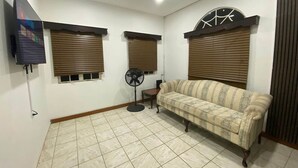 Una sala de estar con un sofá, un ventilador y dos ventanas con persianas.