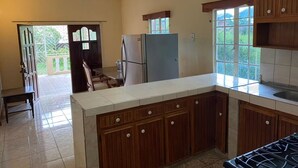 A kitchen with wooden cabinets, a refrigerator, a stove, and a window. - Still Point Guesthouse - Premium Two Bedroom (Crown Point)