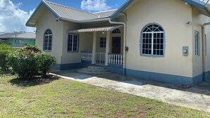 A two-story house with a covered porch, a small garden, and a clear blue sky. - Still Point Guesthouse - Premium Two Bedroom (Crown Point)
