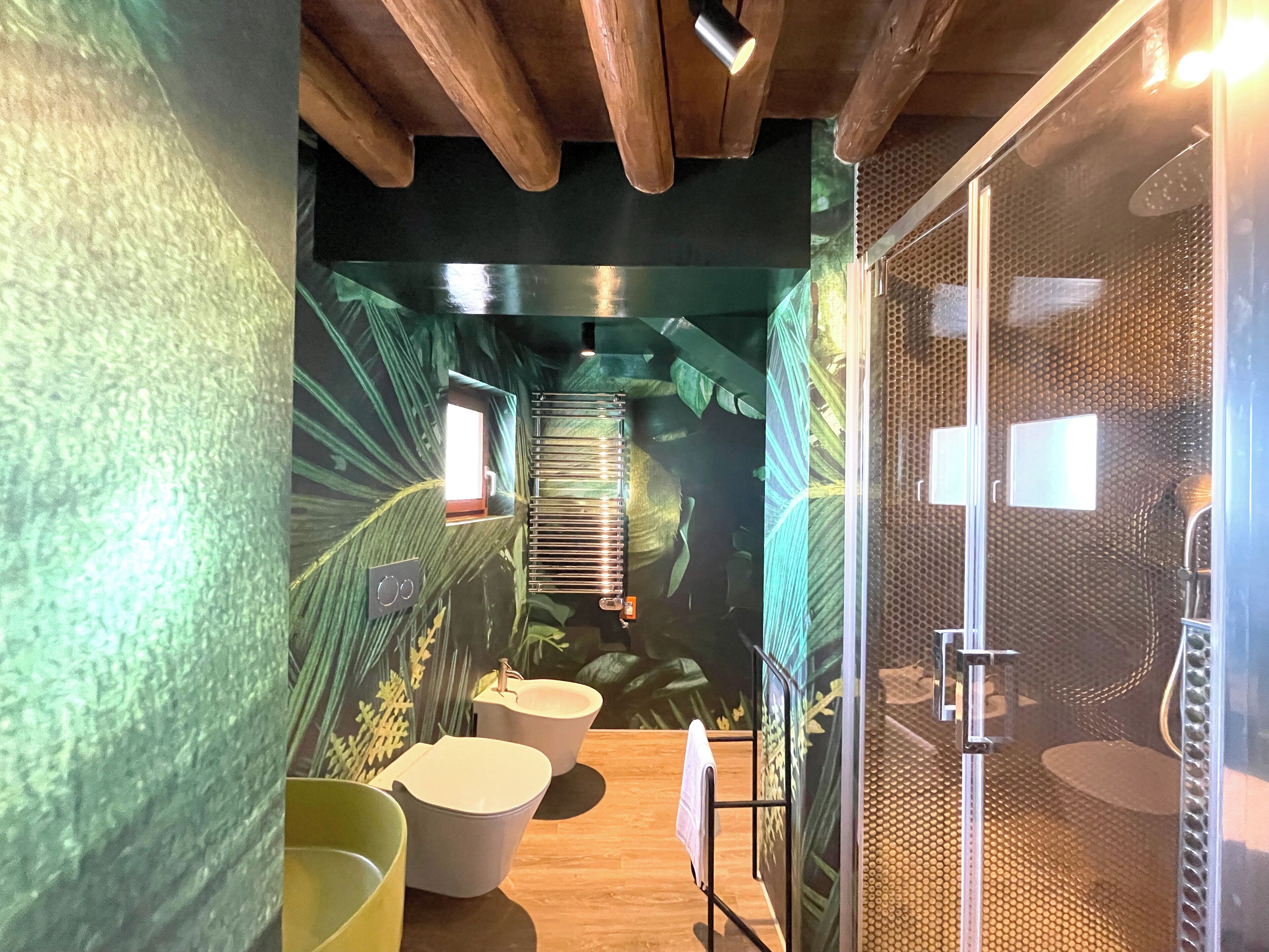 A bathroom with a shower, toilet, and sink, featuring a tropical mural and wooden ceiling beams.