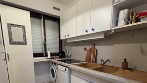 Een praktische keuken met een wasmachine, een spoelbak en een raam met zonwering.