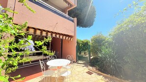 Een terras met een ronde tafel en stoelen, een overdekte zithoek en uitzicht op een gebouw met een balkon.