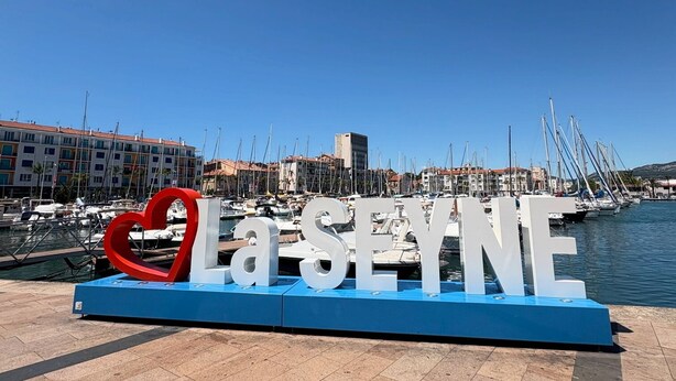Een jachthaven met boten, een groot bord met de tekst 'Casey' en een sculptuur in de vorm van een hart.
