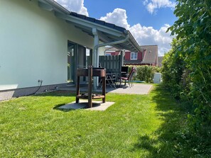 Ein Haus mit Terrasse, Stuhl, Tisch und Garten.