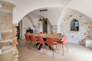 Un comedor con mesa de madera, sillas rojas, paredes de piedra y chimenea de piedra.