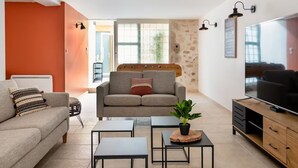 A modern living room with a sofa, two coffee tables, a TV, and a stone accent wall. - Authentic house and private spa for 18 people (La Baume-de-Transit)
