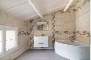 Un baño con tocador blanco, una bañera grande y una zona de ducha con azulejos.