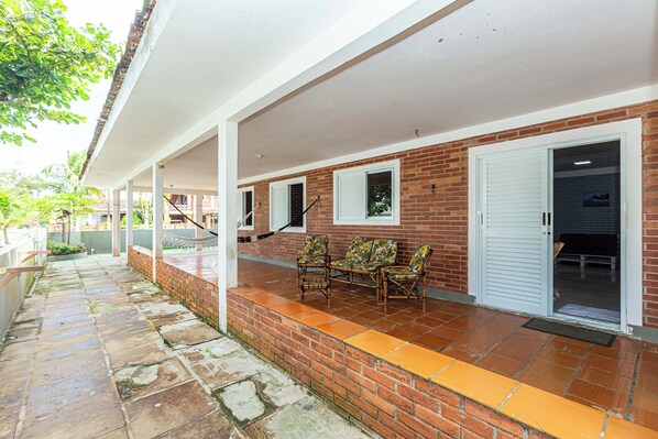A covered outdoor area with a brick wall, a white door, and a set of wooden chairs.