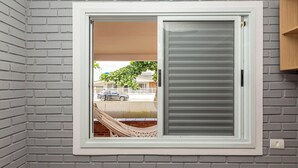 Una ventana con marco blanco y una puerta corrediza de vidrio, empotrada en una pared de ladrillo.