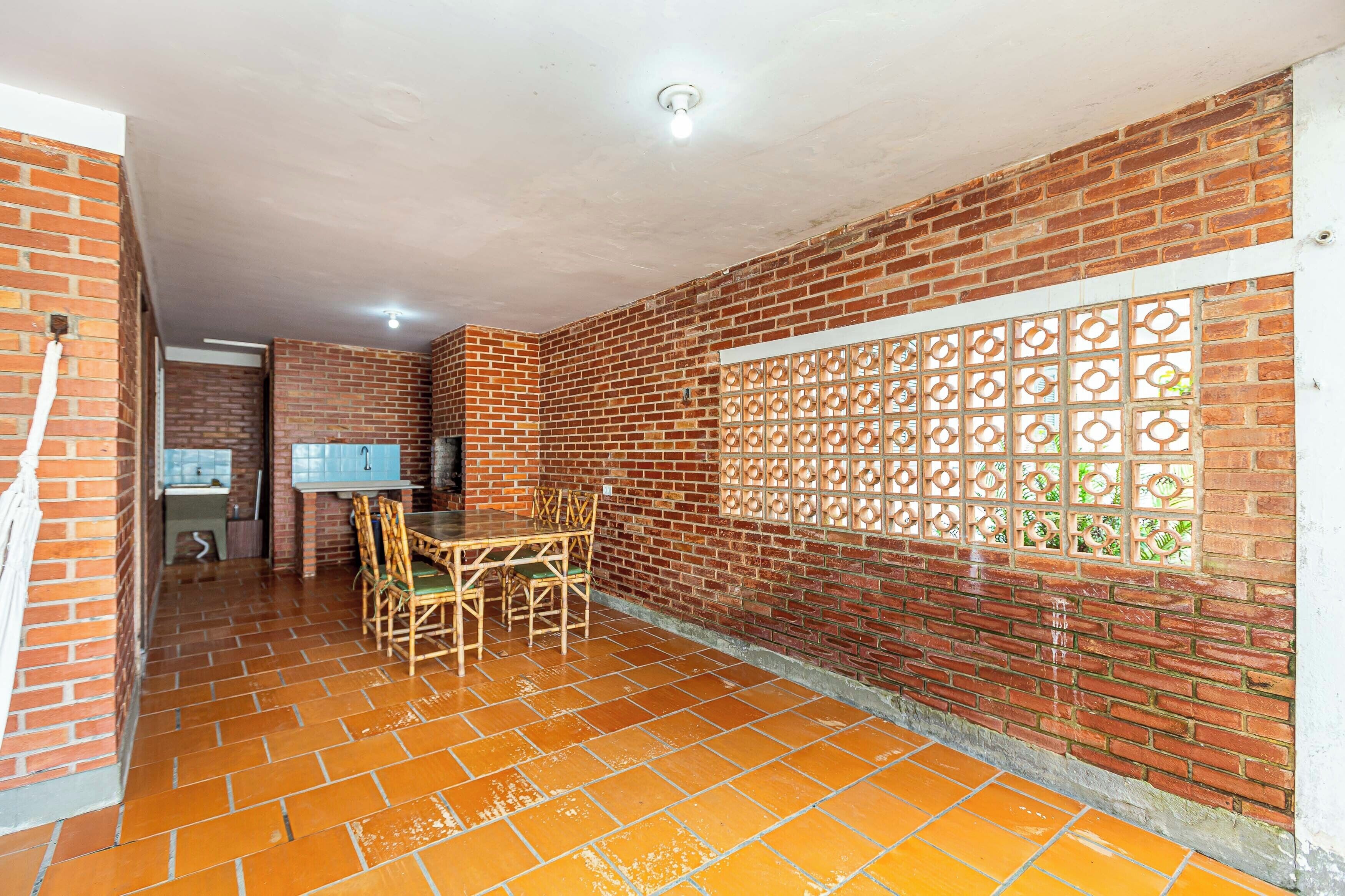 A room with a brick wall, a window with a decorative grille, a tiled floor, and a table with chairs.