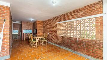 A room with a brick wall, a window with a decorative grille, a tiled floor, and a table with chairs.