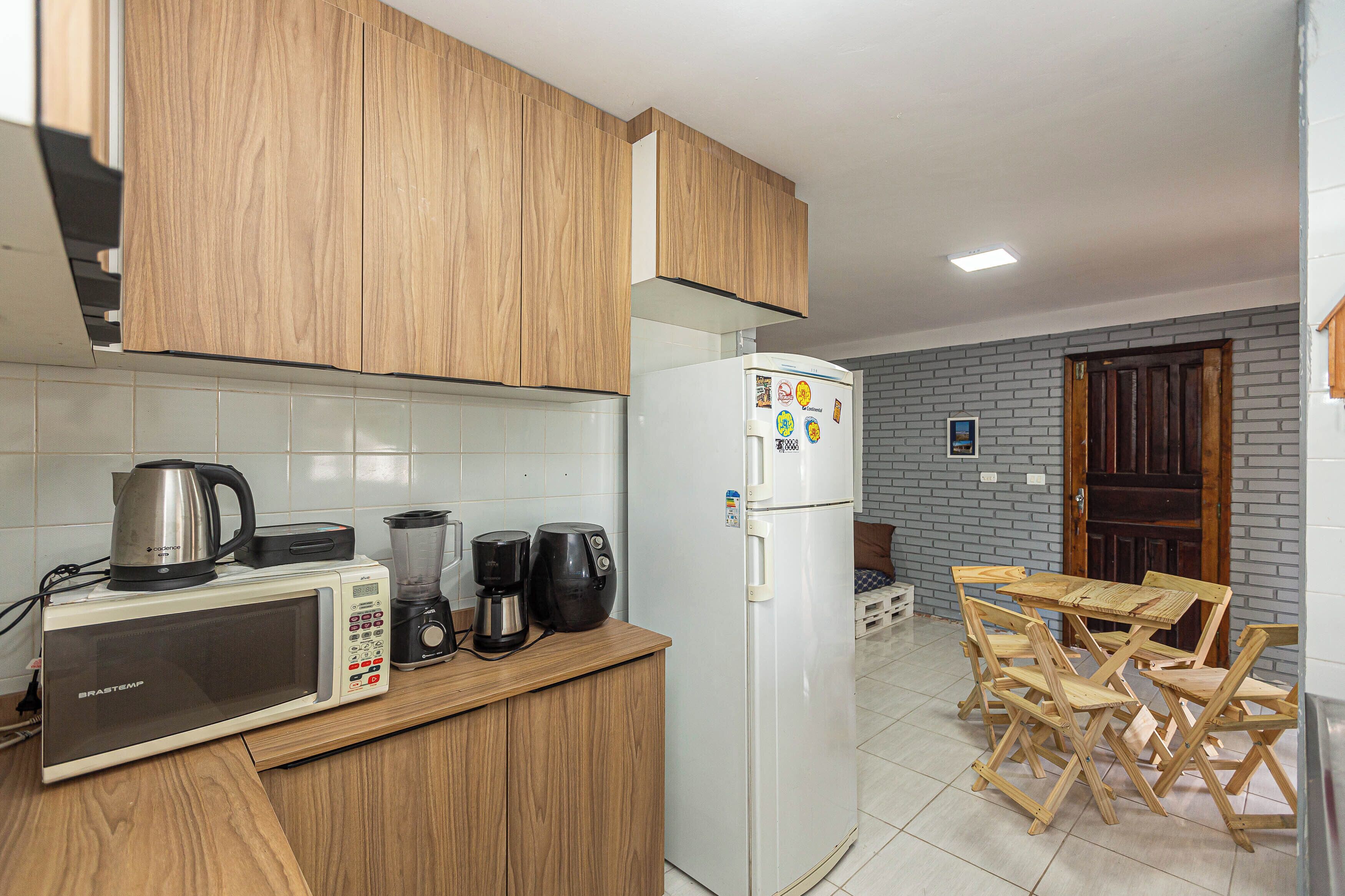 Una cocina con armarios de madera, un refrigerador blanco, un microondas, una cafetera y una licuadora. Hay una mesa de madera y sillas en la zona de comedor.