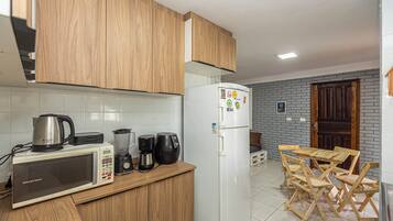 Una cocina con armarios de madera, un refrigerador blanco, un microondas, una cafetera y una licuadora. Hay una mesa de madera y sillas en la zona de comedor.