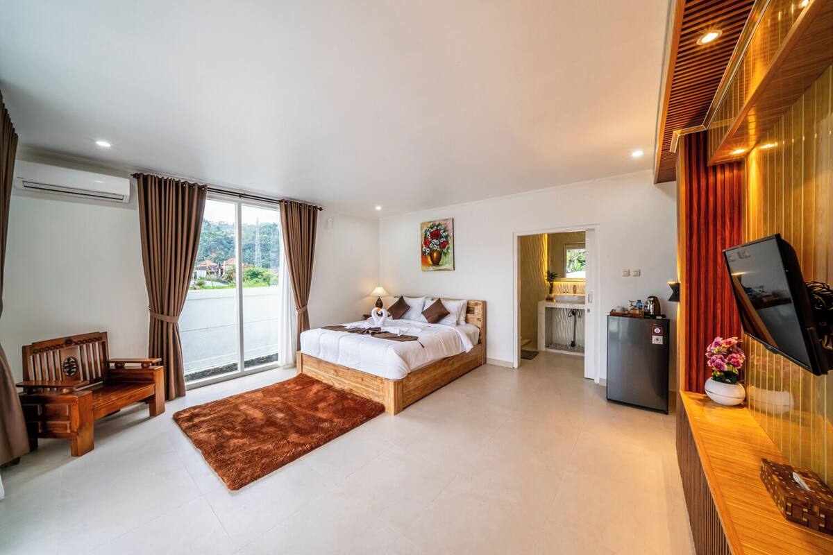 Een moderne hotelkamer met een groot bed, een bureau, een televisie en uitzicht op het omliggende landschap.