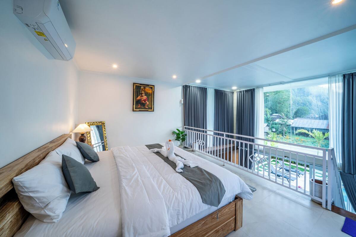 Een moderne hotelkamer met een groot bed, een balkon en uitzicht, en een schilderij aan de muur.