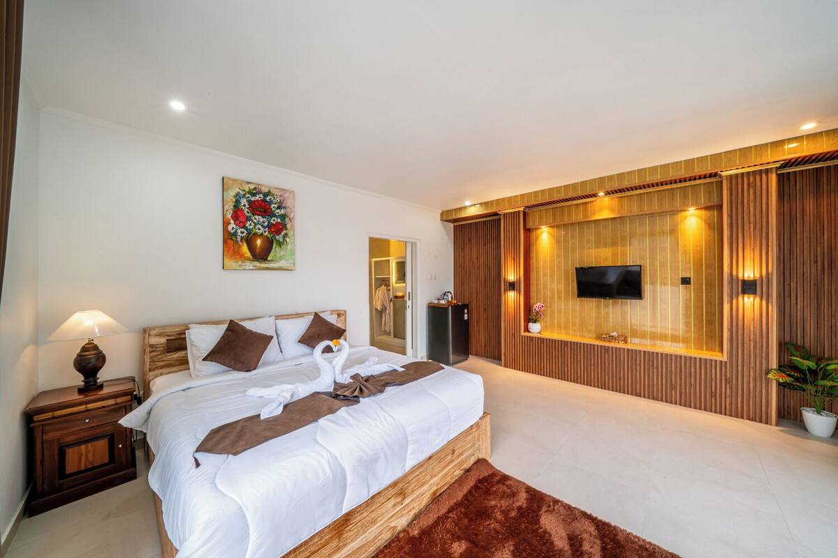 Une chambre d’hôtel moderne avec un grand lit, un téléviseur à écran plat fixé au mur, un mur décoratif en bois et une petite plante en pot.